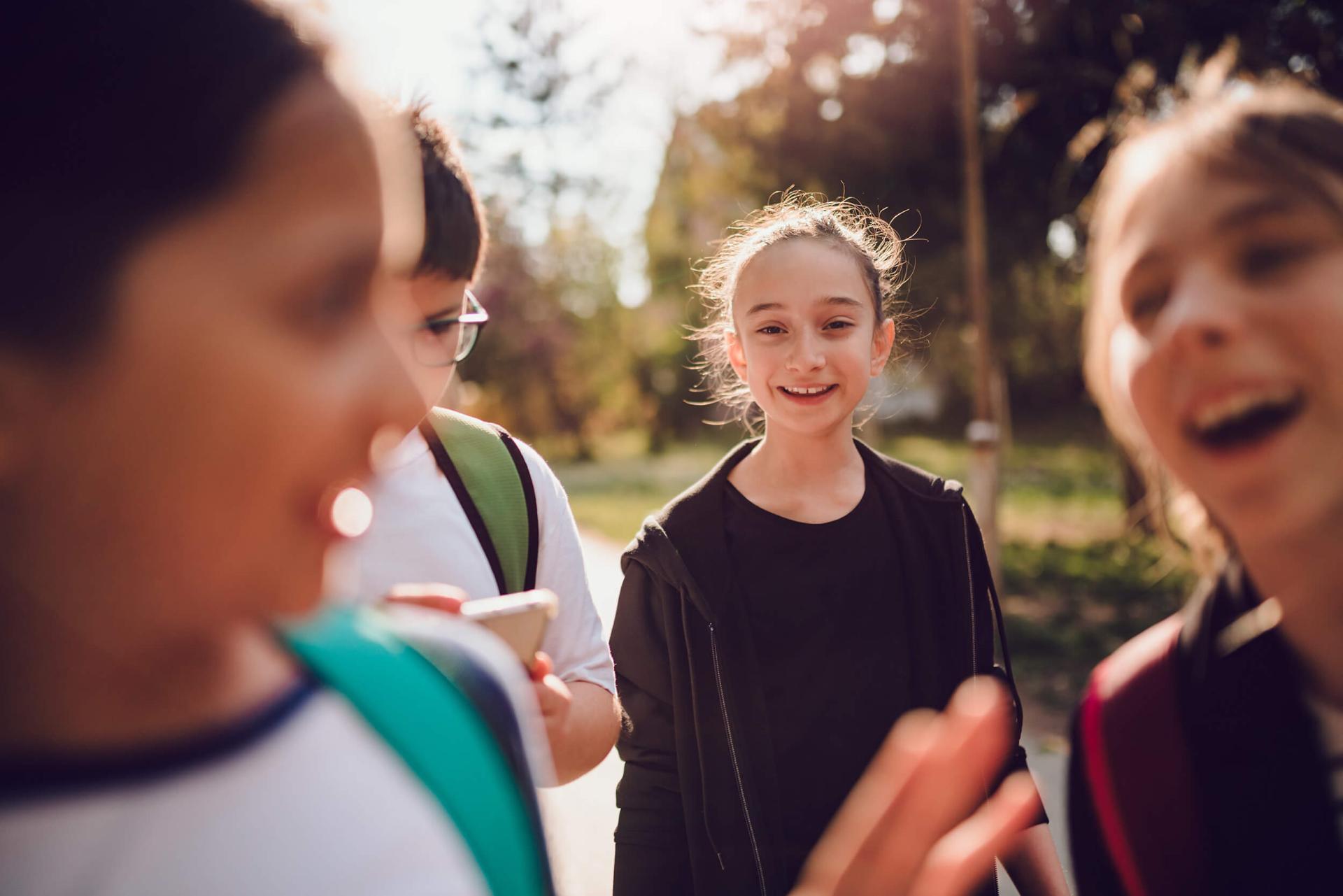 Group of smiling children outdoors, one holding a smartphone. Warm sunlight filters through trees, creating a joyful and carefree atmosphere.