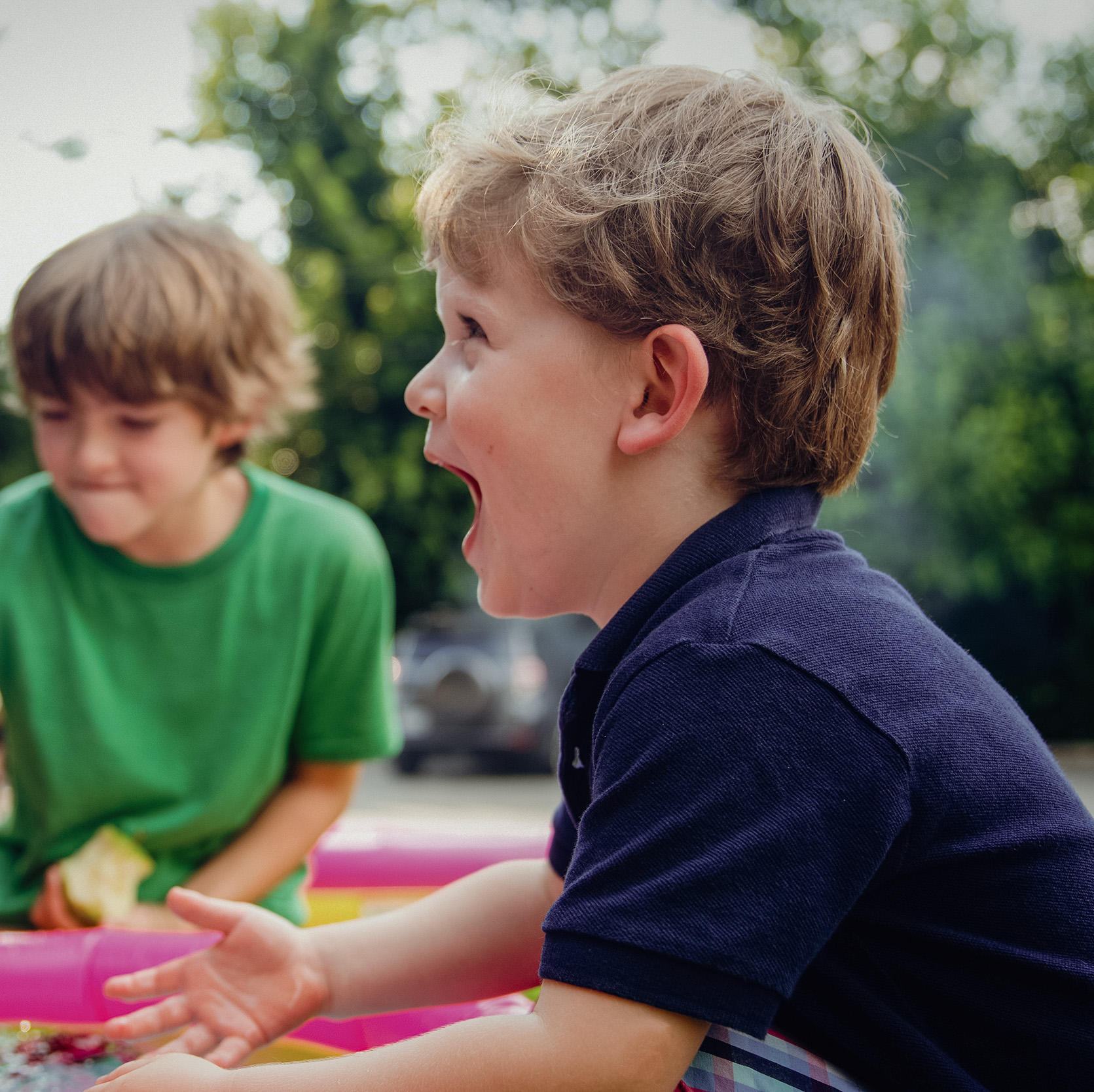 Two boys playing with an inflatable pool outdoors.